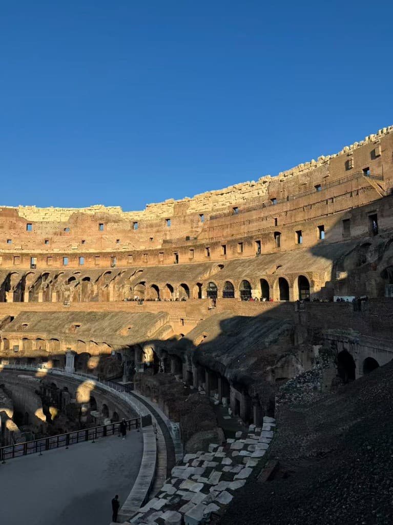 Interior of the Colosseum with stone arches and tiers under a blue sky, Rome, Italy