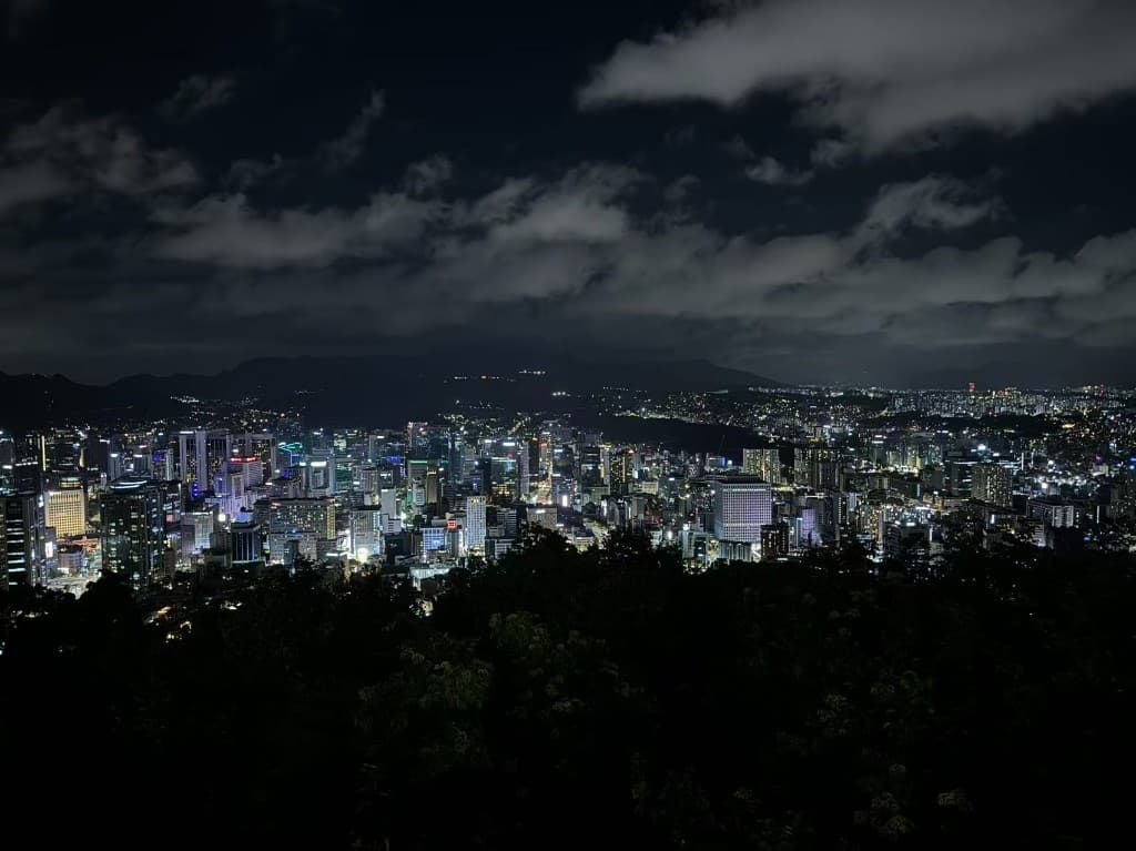 Seoul skyline at night with lit towers, dark hills in the foreground and distant mountains, South Korea